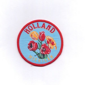 May include: A blue and red embroidered patch with the text "Holland Michigan" and a bouquet of yellow and red tulips.