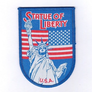 May include: A blue and white embroidered patch featuring the Statue of Liberty and the words "Statue of Liberty" and "U.S.A."