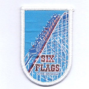 May include: A blue and white embroidered patch with the words "Six Flags Over Georgia" and a depiction of a roller coaster.