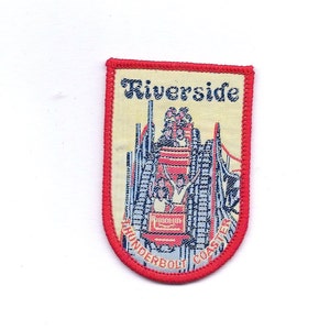 May include: A vintage embroidered patch featuring a colorful illustration of a rollercoaster called "Thunderbolt Coaster" at Riverside amusement park. The patch has a red border and the text "Riverside" in black.