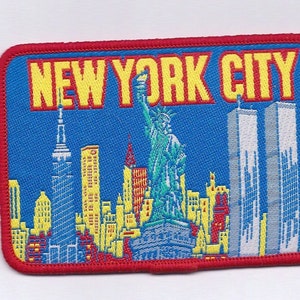 May include: A red, white, and blue embroidered patch with the text "NEW YORK CITY". The patch features a skyline of New York City, including the Statue of Liberty and the Twin Towers.