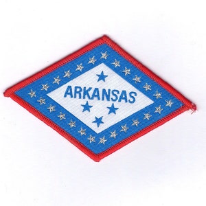May include: A blue and red diamond-shaped patch with the word "ARKANSAS" in white lettering and five silver stars. The patch has a white background with a blue border and a red border.