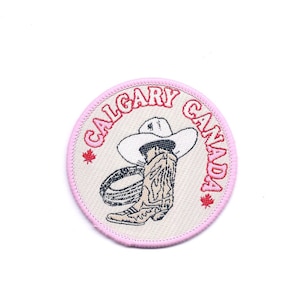 May include: An embroidered patch with a pink and red border, featuring a cowboy boot and hat, and the text "CALGARY CANADA" with a maple leaf on each side.