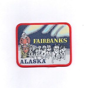 May include: A blue and red embroidered patch with the text "FAIRBANKS ALASKA" in yellow. The patch features a person in a red and white coat riding a dog sled with a team of dogs.