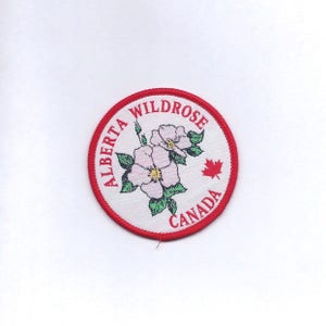 May include: A white circular patch with a red border. The patch features a pink wild rose with green leaves and the text "Alberta Wildrose Canada" in red.
