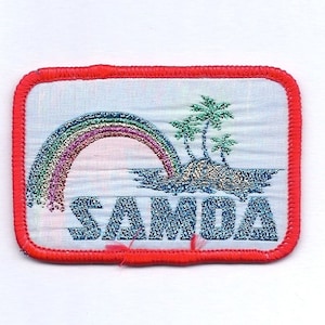 May include: A red-bordered patch with a white background featuring a rainbow arching over a small island with palm trees. The word "SAMOA" is embroidered in blue with a glittery effect.