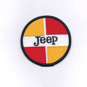May include: A round, embroidered patch with a black outline. The patch is divided into four sections: two yellow, one red, and one white. The word "Jeep" is embroidered in black on the white section.