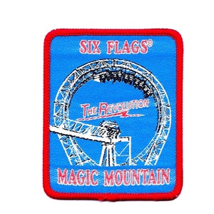 May include: A blue and red embroidered patch with the text "Six Flags® Magic Mountain" and a white outline of a roller coaster called "The Revolution".