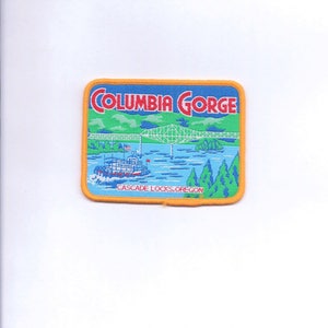 May include: A yellow and blue embroidered patch with the text "Columbia Gorge" in red letters. The patch depicts a bridge over a river with a steamboat and trees. The text "Cascade Locks, Oregon" is at the bottom of the patch.