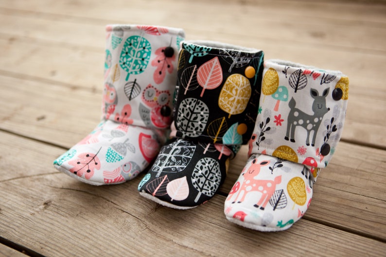 May include: Three pairs of baby booties with different woodland animal and leaf patterns. The booties are made of soft fabric and have a fold-over cuff.