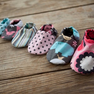 May include: Six pairs of baby shoes in various colours and patterns, including pink with white polka dots, blue with a bird design, and a multi-coloured striped pattern.