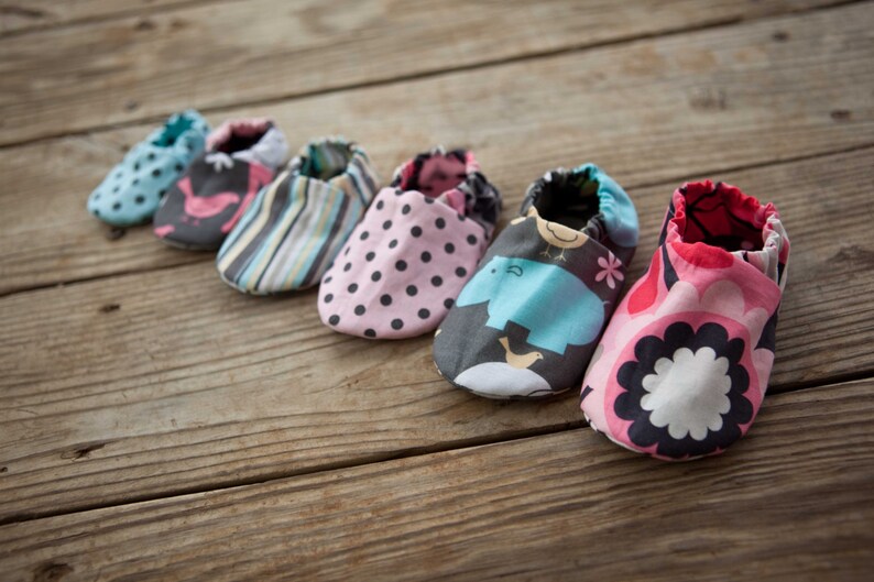 May include: Six pairs of baby shoes in various colours and patterns, including pink with white polka dots, blue with a bird design, and a multi-coloured striped pattern.