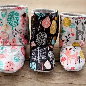 May include: Three pairs of baby booties with different woodland animal and leaf patterns. The booties are made of soft fabric and have a fold-over cuff.