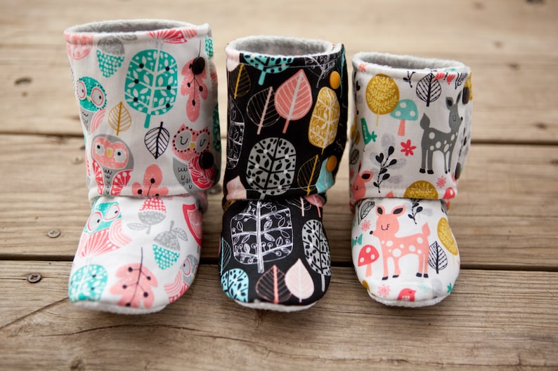 May include: Three pairs of baby booties with different woodland animal and leaf patterns. The booties are made of soft fabric and have a fold-over cuff.