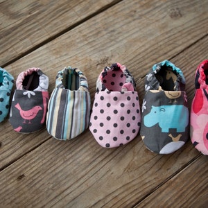 May include: Six pairs of baby shoes in various colours and patterns, including polka dots, stripes, birds, and hippos. The shoes are made of fabric and have a soft, comfortable feel.