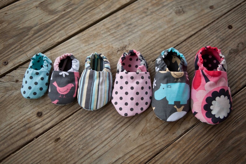 May include: Six pairs of baby shoes in various colours and patterns, including polka dots, stripes, birds, and hippos. The shoes are made of fabric and have a soft, comfortable feel.