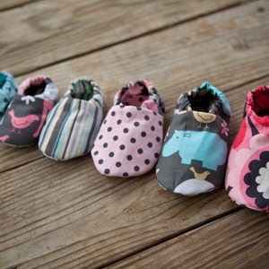 May include: Six pairs of baby shoes in various colourful patterns. The shoes are made of fabric and have a soft, comfortable feel. The patterns include polka dots, stripes, birds, and hippos.