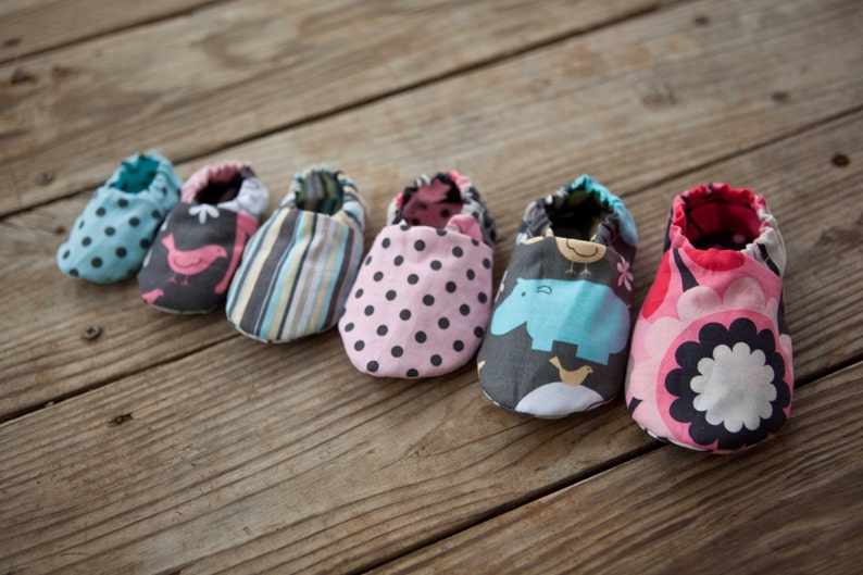 May include: Six pairs of baby shoes in various colourful patterns. The shoes are made of fabric and have a soft, comfortable feel. The patterns include polka dots, stripes, birds, and hippos.
