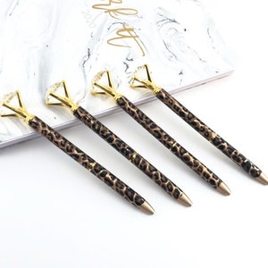 May include: Four gold pens with a leopard print design and a clear diamond-shaped top.