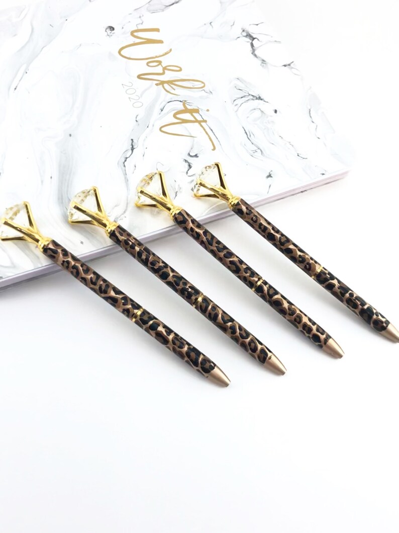 May include: Four gold pens with a leopard print design and a clear diamond-shaped top.