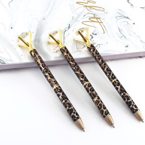 May include: Three gold pens with a leopard print design and a large clear diamond-shaped top.
