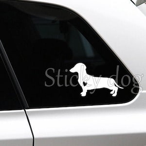 May include: White silhouette of a dachshund dog on a black car window with the text "Sticky Dog" in white.
