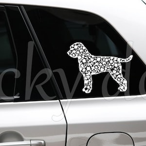 Op de afbeelding: Een witte auto met een zwart-witte hondensilhouet sticker op de achterruit. De sticker is gemaakt van voetafdrukken. De sticker zegt "Stickydog" onderaan.