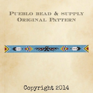 May include: A beaded pattern with a blue background, black, white, red, and yellow beads. The pattern features a bird with outstretched wings and feathers. The text "Pueblo Bead & Supply Original Pattern" and "Copyright 2014" are also included.
