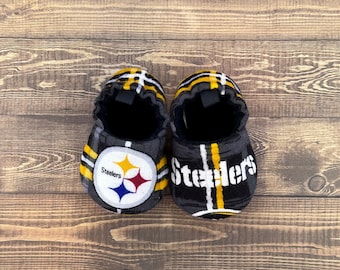 May include: A pair of black and yellow slippers with a Steelers logo and the word "Steelers" on them.