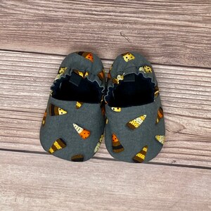 Puede incluir: Un par de zapatos grises para bebé con estampado de maíz dulce. Los zapatos tienen una banda elástica negra alrededor del tobillo.
