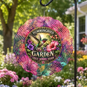 May include: A circular metal wind spinner featuring a scalloped edge with a vibrant pink, purple, and teal gradient. The center displays a hummingbird in flight near flowers with the text Hummingbird Garden and Grace Beauty Bloom.