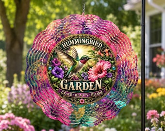 May include: A circular metal wind spinner featuring a scalloped edge with a vibrant pink, purple, and teal gradient. The centre displays a hummingbird in flight near flowers with the text Hummingbird Garden and Grace Beauty Bloom.