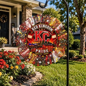 May include: A circular metal wind spinner hanging from a black shepherd's hook. The design features a red and gold color scheme with the text 'RED KINGDOM' and 'PRIDE' surrounding a central 'KC' logo and a Kansas City skyline graphic.
