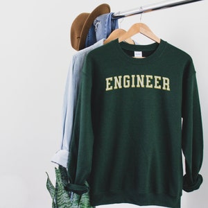May include: A dark green sweatshirt with the word "ENGINEER" printed in gold letters on the front.