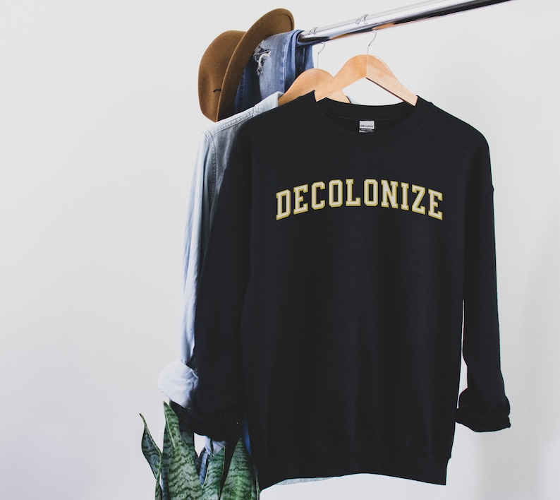 Pu&ograve; includere: Felpa nera con la scritta "DECOLONIZE" in lettere dorate.