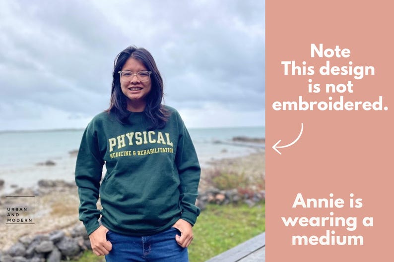 Op de afbeelding: Een groen sweatshirt met de tekst "PHYSICAL MEDICINE & REHABILITATION" in gele letters. Het model draagt maat M.