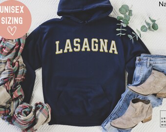 May include: Navy blue hoodie with the word "LASAGNA" in gold lettering. The hoodie has a front pocket and a hood. The image also includes jeans, boots, and a scarf. The text "UNISEX SIZING" is in a pink circle.