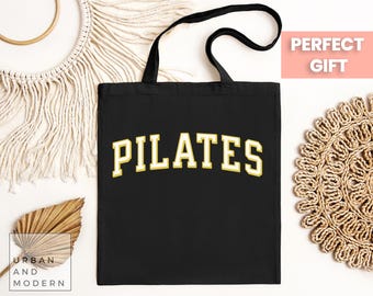 May include: Black tote bag with a gold "PILATES" graphic. The bag has a long handle and is made of canvas.