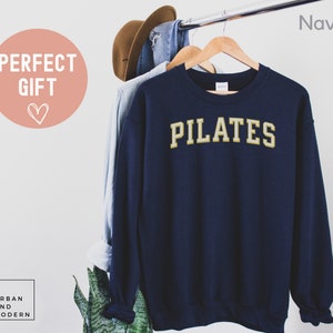 May include: Navy blue sweatshirt with the word "PILATES" in gold lettering.