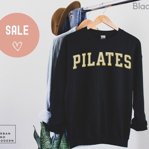 May include: Black sweatshirt with the word "PILATES" in gold lettering.