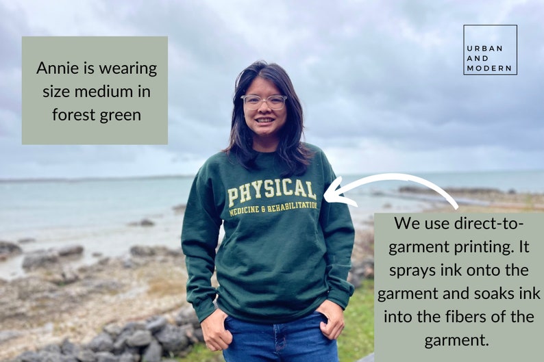 May include: A forest green sweatshirt with the text "PHYSICAL MEDICINE & REHABILITATION" printed on the front. The sweatshirt is being worn by a person with dark hair and glasses. The text "URBAN AND MODERN" is visible in the upper right corner of the image.