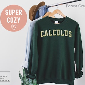 May include: Forest green sweatshirt with the word "CALCULUS" in a gold, collegiate-style font. The sweatshirt is hanging on a wooden hanger. The words "SUPER COZY" and a heart are in a pink circle in the upper left corner.