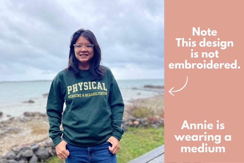 May include: A dark green sweatshirt with the text "PHYSICAL MEDICINE & REHABILITATION" in gold lettering. The design is not embroidered. The person in the image is wearing a medium.