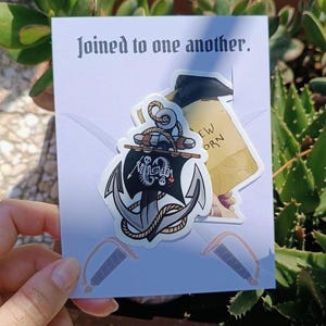 May include: A sticker set featuring a pirate theme. The main sticker is an anchor with a black sail and skull design. The text "Joined to one another" is printed on the card. Includes a sticker with the text "EW ORN".