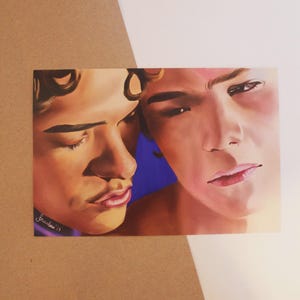 Può includere: Una stampa artistica raffigurante due giovani con toni della pelle caldi e capelli castani ricci. L'opera d'arte ha uno stile morbido e pittorico, con una figura che guarda intensamente e l'altra con gli occhi chiusi. Lo sfondo è un mix di blu e toni caldi.