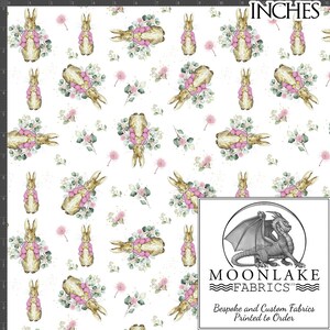 May include: White fabric featuring a repeating pattern of watercolour bunnies adorned with pink bows and floral arrangements in pink and green. The word "INCHES" is at the top. The Moonlake Fabrics logo is in the bottom right corner.