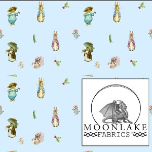 May include: A blue and white fabric with a repeating pattern of Peter Rabbit characters. The fabric features a light blue background with white outlines of Peter Rabbit, carrots, peas, and flowers. The text "MOONLAKE FABRICS" is in the lower right corner of the image.