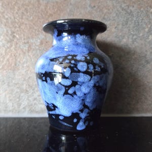 May include: A small ceramic vase with a dark blue rim and base, and a vibrant blue and black speckled pattern on the body. The vase has a rounded shape and a narrow neck, suitable for displaying small flowers or as a decorative piece.