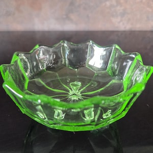 May include: A small, clear glass dish with a vibrant green rim and accents. The dish has a starburst pattern in the center and a scalloped edge. The dish is approximately 12.7 cm in diameter.
