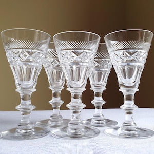 May include: A set of five clear crystal wine glasses. Each glass features detailed diamond and line patterns, a stemmed base, and a wide, angled rim. The glasses are arranged on a white surface.